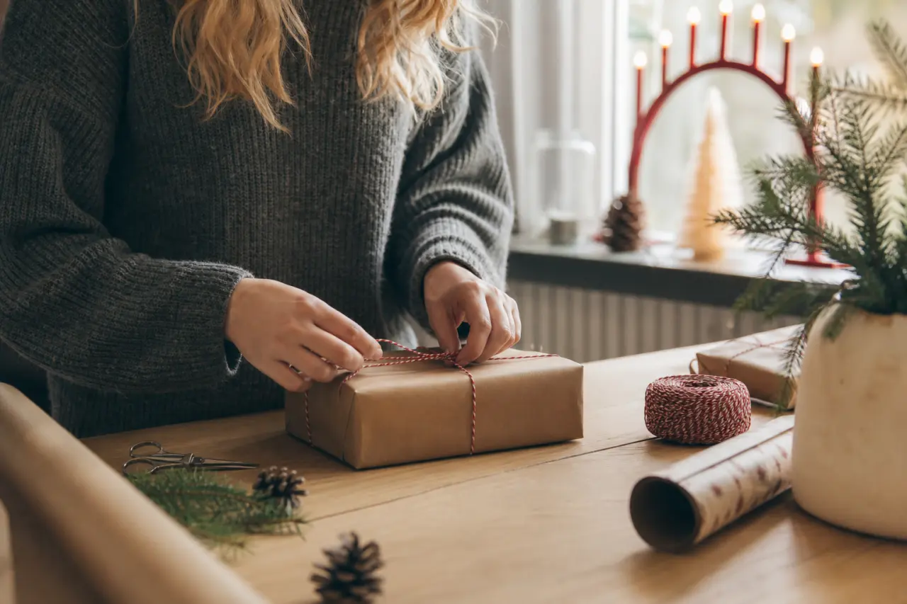 händer som slår in ett julklappspaket i papper på ett bord